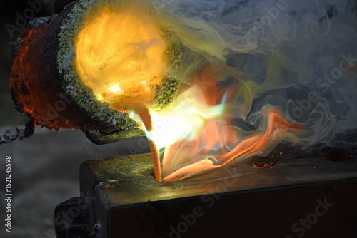 flüssiges Metall gießen aus rotglühendem, rauchendem Schmelztiegel mit lodernden Flammen