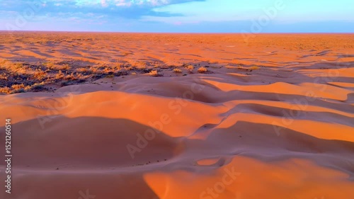 Sunset paints the dunes in vivid orange and purple tones. Aerial drone view showcases the vast scale and natural beauty of the desert