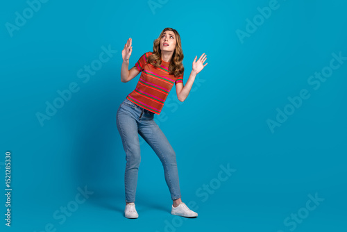 Casual young woman in a striped shirt gesturing humorously against a vibrant blue background, showcasing cheerful and stylish fashion