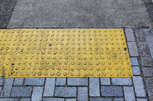 Yellow blocks of tactile paving for blind handicap. Tactile pavement for the visually impaired close up background. Texture of blue and brown square paving tile with Braille blocks in the street.