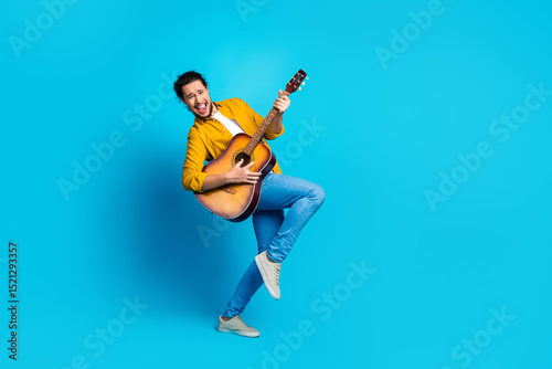 Joyful man in casual yellow shirt playing guitar on blue background showcasing music and happiness as lifestyle