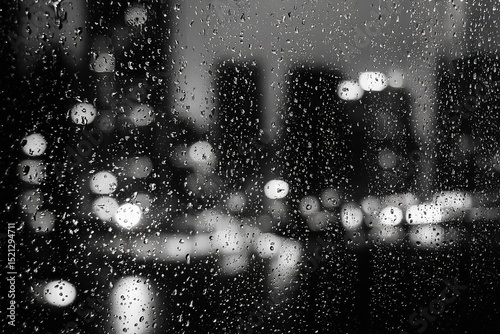 Rain droplets on a window in monochrome with blurred cityscape background

