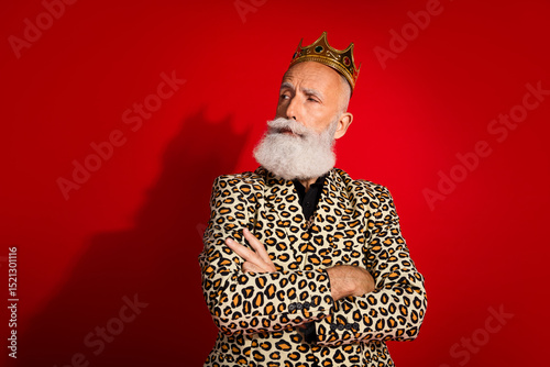 Confident senior man with crown and leopard print outfit on vibrant red backdrop embodying extravagance and style photo