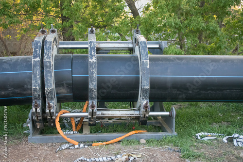 Large black pipeline installation process in a green area during daylight hours