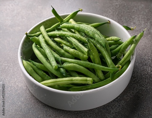 fresh green beans with water drops in a white bowl on a gray background for commercial use