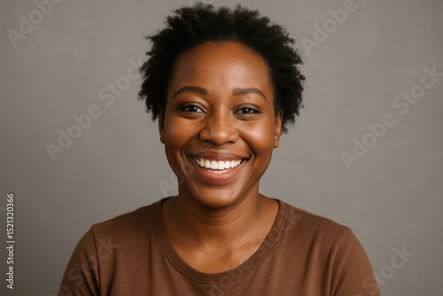 Smiling woman with natural hair displays joy against a neutral backdrop in a warm lighting setting