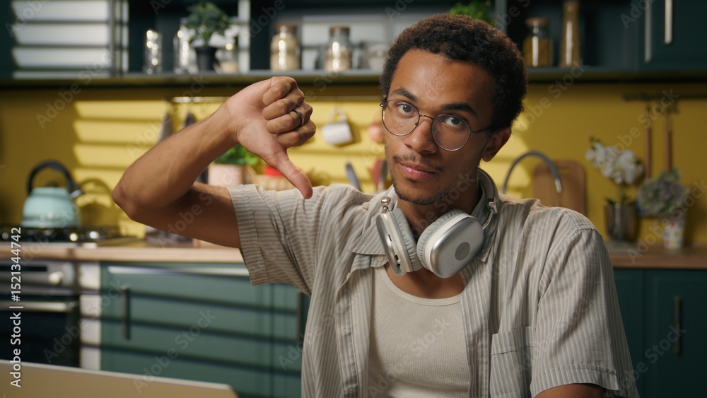 Obraz premium Serious guy African American man male student gen z freelancer businessman distant education laptop work at home kitchen showing thumb down gesture negative dislike bad studying learning in university