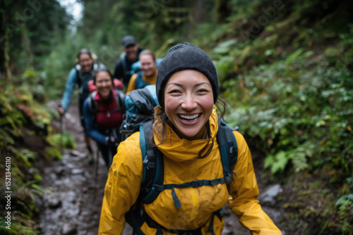Group of joyful hikers, wearing backpacks, navigating a muddy trail while relishing their outdoor adventure in a vibrant, lush forest filled with greenery and towering trees