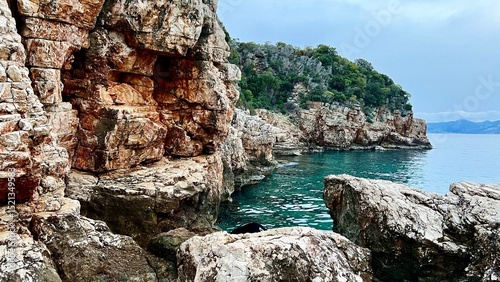 Photography Steep rocky cliffs with textured orange and white stone rise above calm turquoise water
