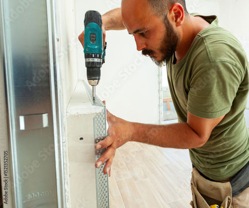 Construction worker installing metal corner bead on drywall with cordless screwdriver