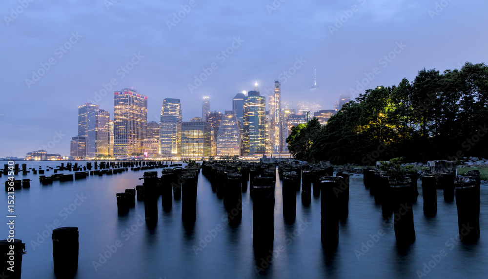 Fototapeta premium new york city skyline at dusk with old abandoned wood pier barge poles long exposure downtown manhattan blue fog hour foggy hazy haze atmosphere rain weather