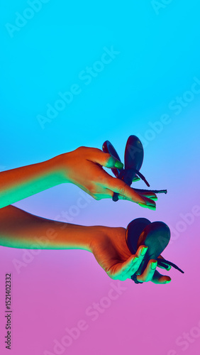 Tableau sur toile Pair of hands rhythmically moving castanets under blue and purple neon light against gradient studio background