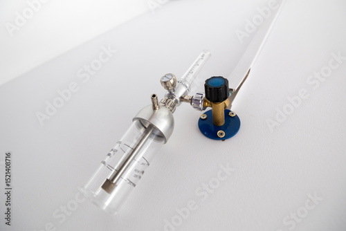 An oxygen flow meter with a humidifier bottle is mounted on a white wall, part of an oxygen hub, ready for use in a hospital intensive care unit.