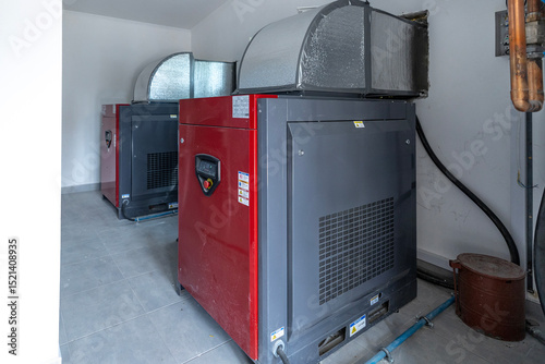 Two large industrial screw compressors, capable of 3220 liters per minute, stand in a utility room with insulated ductwork overhead, showcasing industrial machinery.