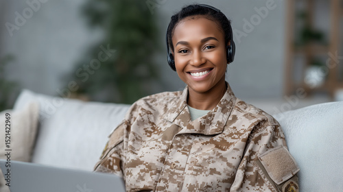 Happy military woman in uniform working from home on a laptop, smiling while wearing headphones and video chatting with her family. Cozy home office setup. military woman remote wo