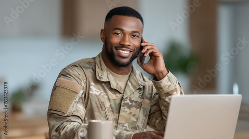 Mixed race military soldier in uniform standing at a kitchen counter using a laptop and talking on a cell phone. Morning light, casual home setting with coffee mug nearby. mixed ra