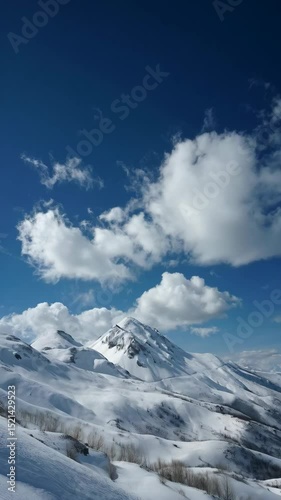 Snowy mountain range landscape under a clear blue sky with white clouds on a bright winter day, outdoor scenery.