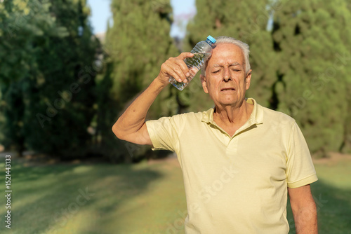 Elderly man placing cold water bottle on forehead to relieve heat stroke symptoms during summer heat
