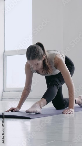 Young beautiful brunette girl in sportswear doing warming up exercises in a bright sport studio. Healthy motivated woman stretching legs indoors. Fitness, yoga, welness. Slow motion cinematic shot