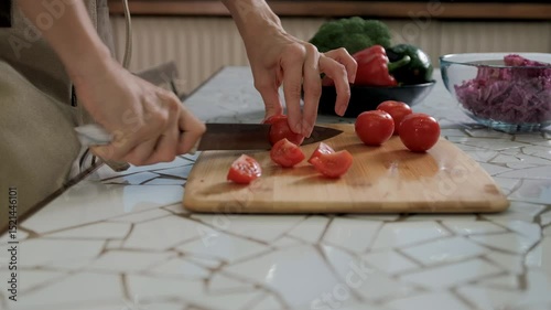 Chef is slicing cherry tomatoes on a wooden board, with a bowl of vegetables in the background