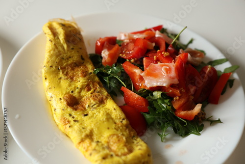 Healthy breakfast with omelette and fresh salad with cherry tomatoes and arugula, dressed with mustard, honey and olive oil sauce on white plate. Nutritious meal with protein and fiber. Ketogenic diet