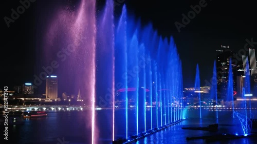 Luminous fountain display dancing with colorful laser lights against dramatic singapore nighttime cityscape