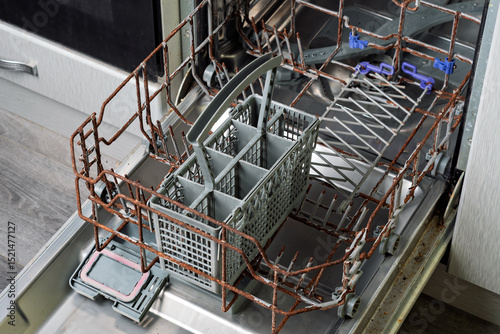 Protective coating of dishwasher rack has cracked and peeled, exposing rusted metal and causing deterioration of the basket frame, symbolizing appliance wear.