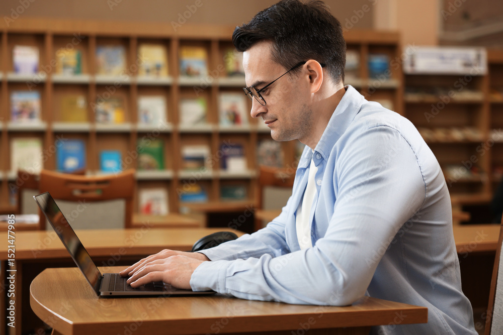 Obraz premium Man working on laptop at desk in public library