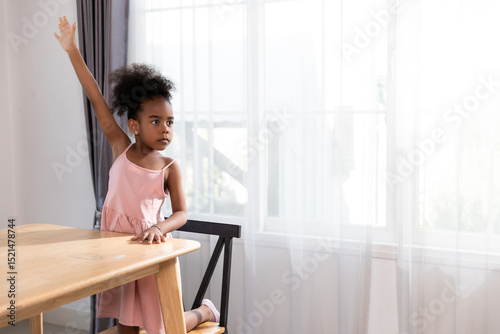 Confident young African girl raising her hand to answer a question in class, showing eagerness to participate and learn in a bright, engaging educational environment.
