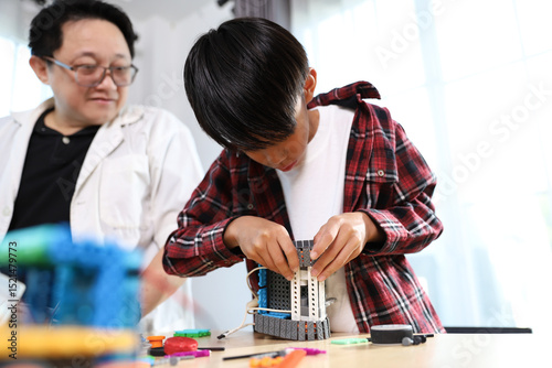Stem education class, A young boy is deeply engrossed in assembling a robot from construction blocks, while an adult observes and provides guidance in a learning environment