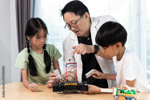 Asian teacher teaching kids robotics and STEM education. Children learn by assembling and controlling a robot car in a fun and engaging classroom environment.