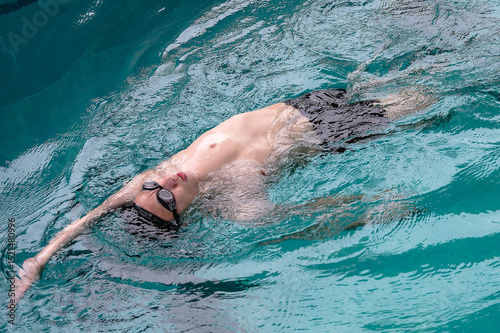 Asian male swimmer swimming backstroke in pool