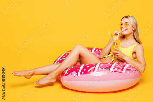 Full body young fun beautiful sexy woman wear bikini swimsuit rest near hotel pool lies on rubber ring drink citrus cocktail isolated on plain yellow background. Summer vacation sea sun tan concept.