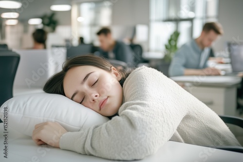 Young woman naps sweetly hugging pillow at her desk in bright open office, capturing peaceful escape during busy workday