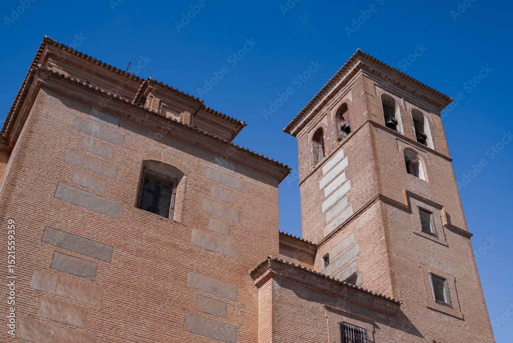 The bell tower of the Church of the Incarnation in Laujar de Andarax, Almeria, Spain, rises gracefully with brick walls, arched windows, and visible bells, set against a vivid blue sky The bell tower of the Church of the Incarnation in Laujar de Andarax, Almeria, Spain, rises gracefully with brick walls, arched windows, and visible bells, set against a vivid blue sky