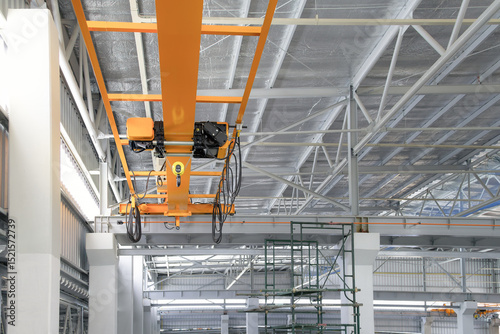 Overhead crane inside factory or warehouse building. Industrial machine or lifting equipment consist of hoist, hook and wire rope move on beam girder structure for manufacturing production plant.
