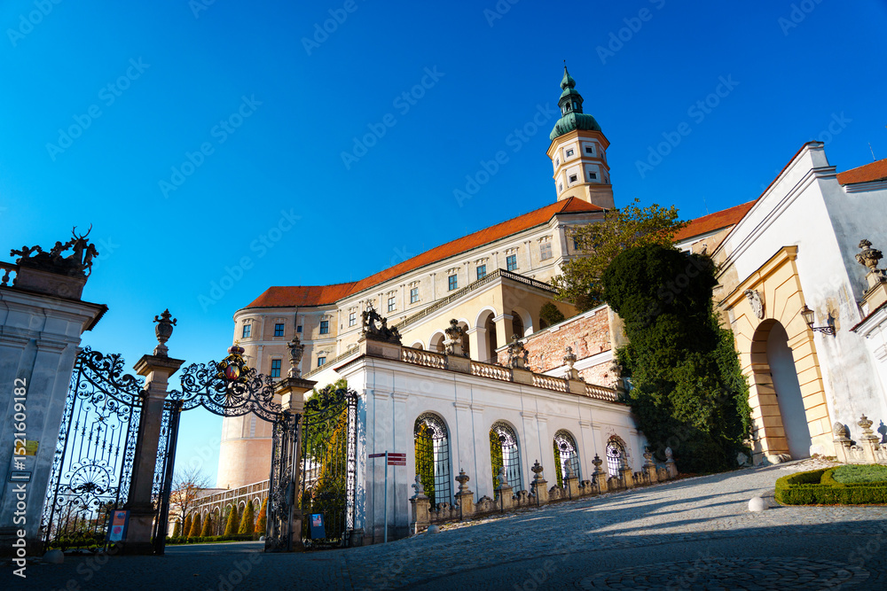 Naklejka premium Baroque Mikulov Castle in South Moravia, Czech Republic, photographed on a sunny day. Historic architecture, ornate gates and vivid blue sky create a striking travel destination image.