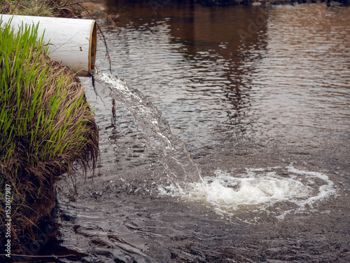 Clean water runs from white plastic pipe into river. Result of water plant work. Keeping nature clean and fighting pollution concept. photo