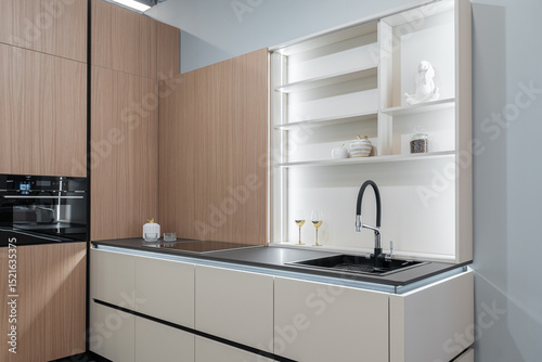 modern built-in kitchen in light color with upper and lower cabinets. glass doors, steel faucet and sink, built-in kitchen appliances. wine glasses on shelves. kitchen unit