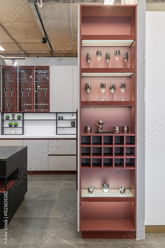 large corner built-in kitchen with upper and lower cabinets. Modern kitchen in light grey with burgundy elements. Upper cabinets with glass doors. built-in appliances. beautiful wine glasses on shelf 