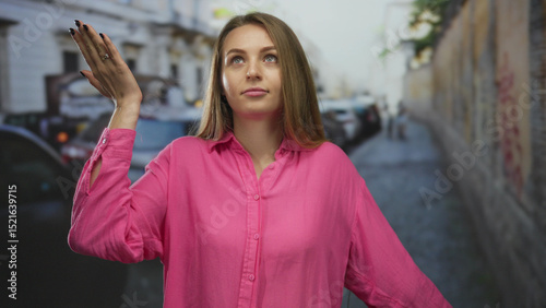 Woman showing frustration and indifference with a hand gesture in a busy city street wearing a vibrant pink shirt outdoors.