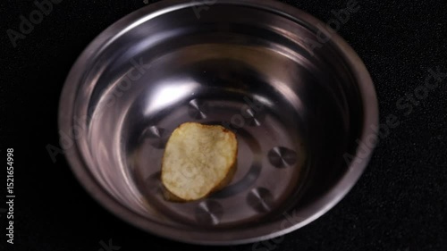 Homemade potato chips spilling out into a metal bowl close-up on a dark background