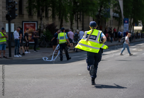 Law enforcement officer in fluorescent safety vest running urgently on city street during daytime patrol, demonstrating emergency response in urban setting