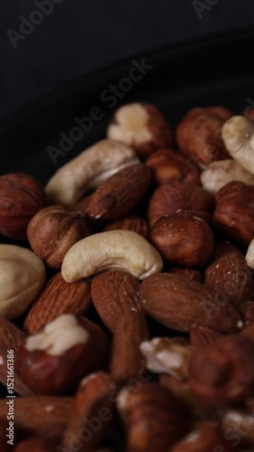 Different nuts on a plate on a black background for a healthy lifestyle, nuts almonds, peanuts, walnuts and cashews 