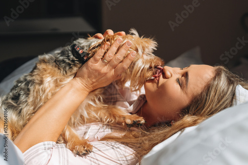 Фотография Woman enjoys affectionate moment with small dog while relaxing on bed in a cozy