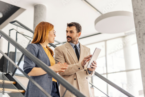 Foto Serious businesspeople descending stairs with tablet in hands and discussing project