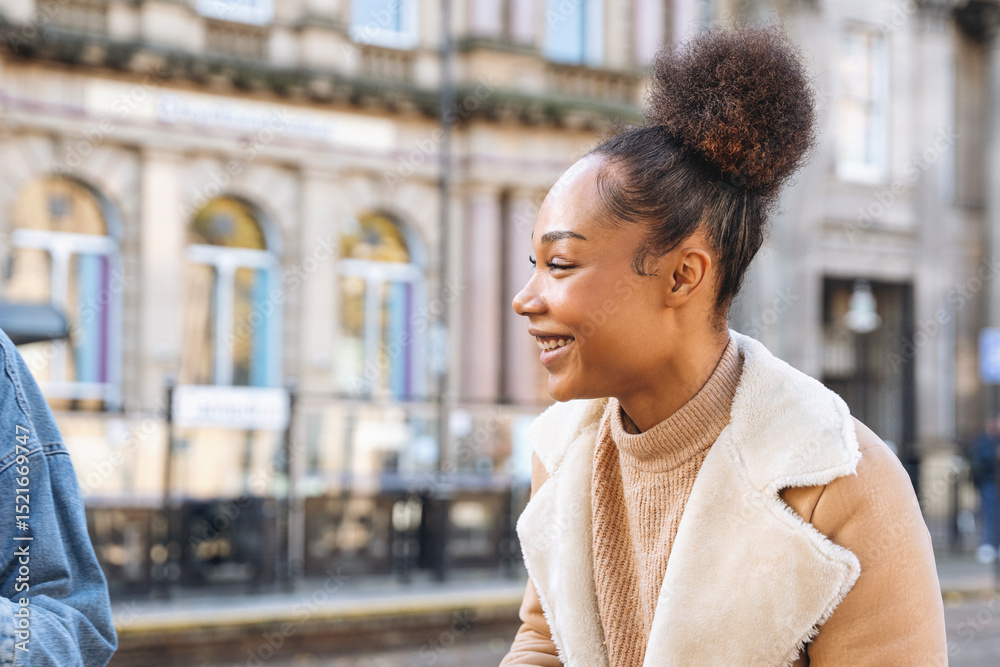 Fototapeta premium Young woman smiling while enjoying conversation outdoors in city street during a sunny day