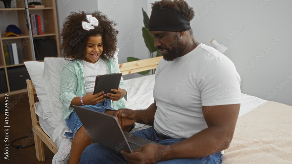 Fototapeta premium Father and daughter sitting on a bed in a cozy room using laptop and tablet, showcasing family bond and digital lifestyle at home.