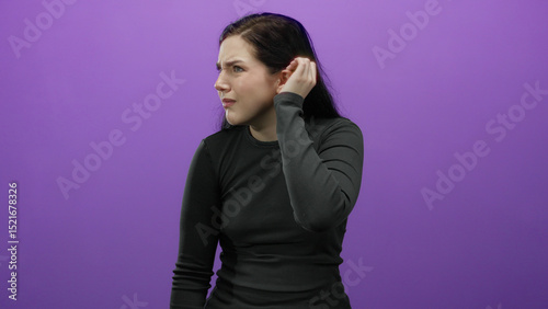 Woman with brunette hair makes listening gestures against purple background expressing curiosity and attentiveness