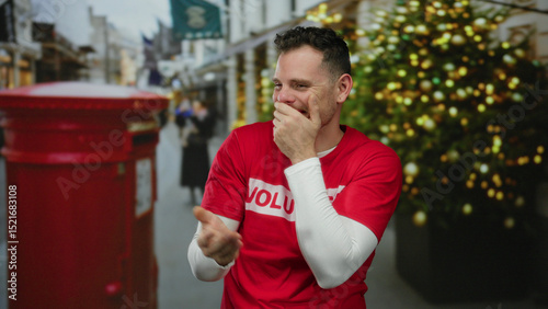 Photography Man laughing joyfully in city street wearing red shirt with holiday decorations and british postbox in background during festive season